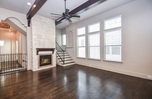 unfurnished living room with beam ceiling, dark hardwood / wood-style flooring, a stone fireplace, and ceiling fan