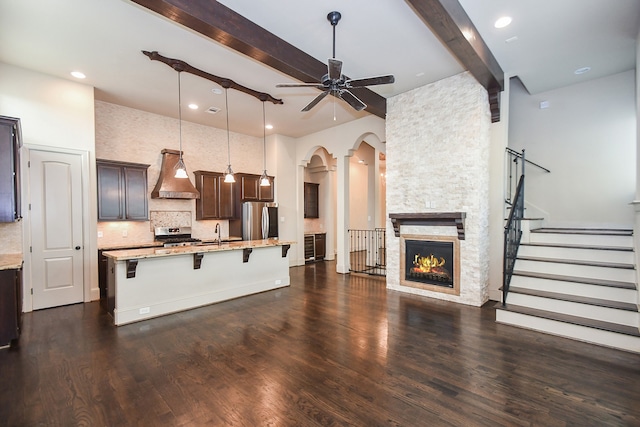 kitchen with appliances with stainless steel finishes, a kitchen breakfast bar, premium range hood, a fireplace, and hanging light fixtures