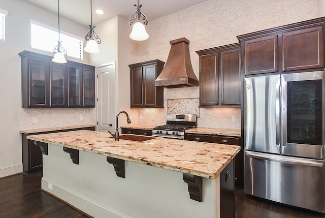 kitchen with sink, stainless steel appliances, premium range hood, pendant lighting, and dark brown cabinets