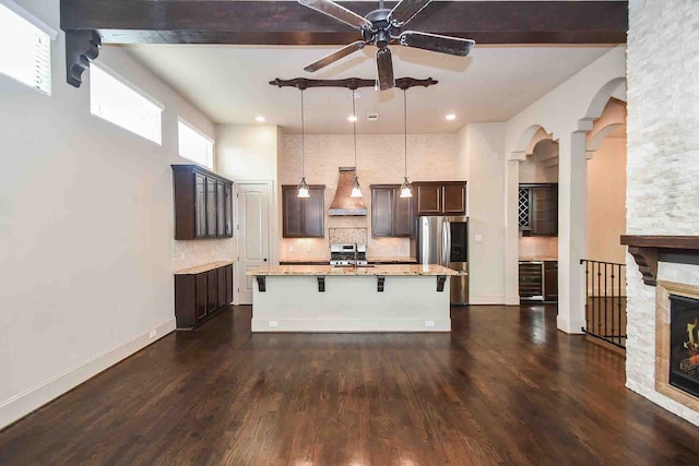 kitchen with hanging light fixtures, wall chimney range hood, stainless steel fridge, a kitchen bar, and a kitchen island