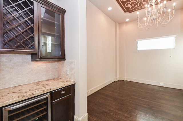 bar with backsplash, dark brown cabinetry, beverage cooler, dark wood-type flooring, and a chandelier