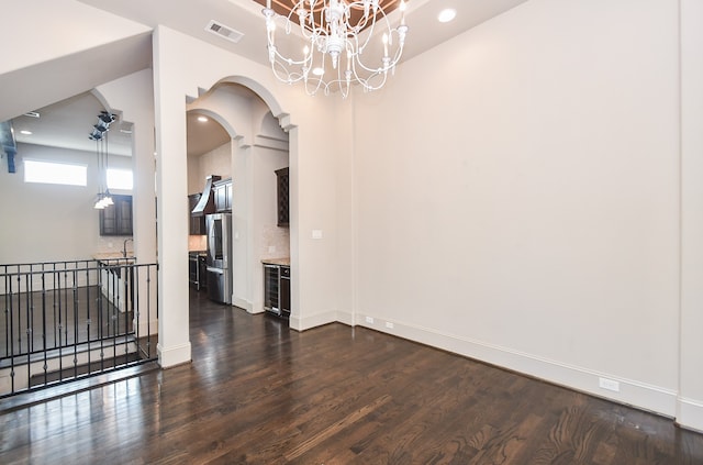 spare room with a chandelier, beverage cooler, and dark wood-type flooring