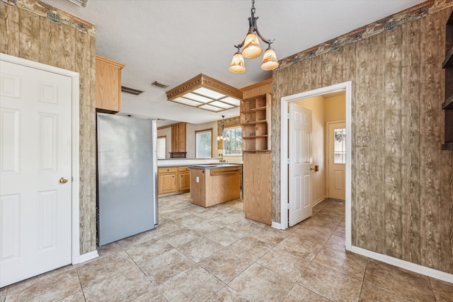 kitchen with pendant lighting, a kitchen island, wooden walls, stainless steel refrigerator, and a notable chandelier