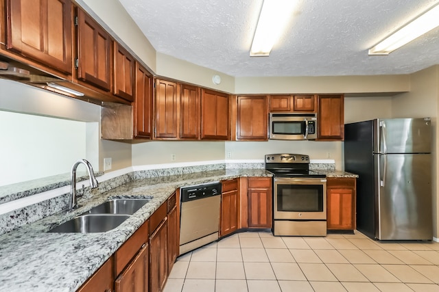 kitchen with light stone counters, light tile patterned floors, sink, a textured ceiling, and appliances with stainless steel finishes