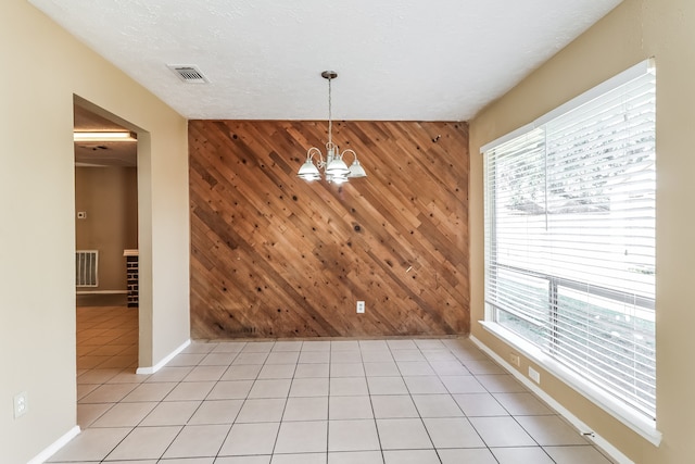 unfurnished dining area with light tile patterned floors, wood walls, a chandelier, and a textured ceiling