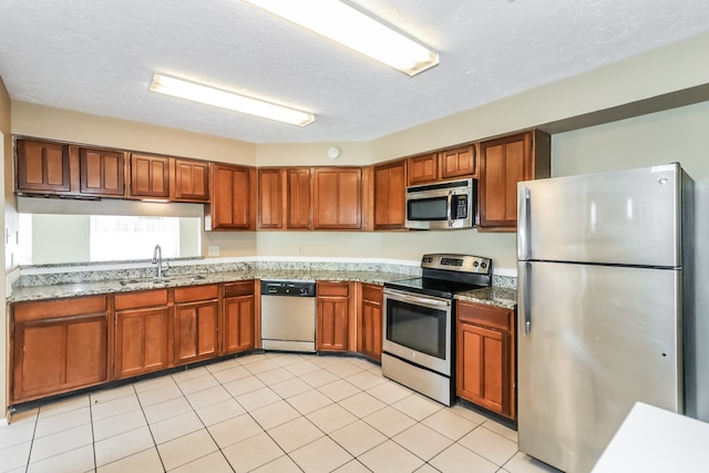 kitchen with stainless steel appliances, sink, light tile patterned floors, and a textured ceiling