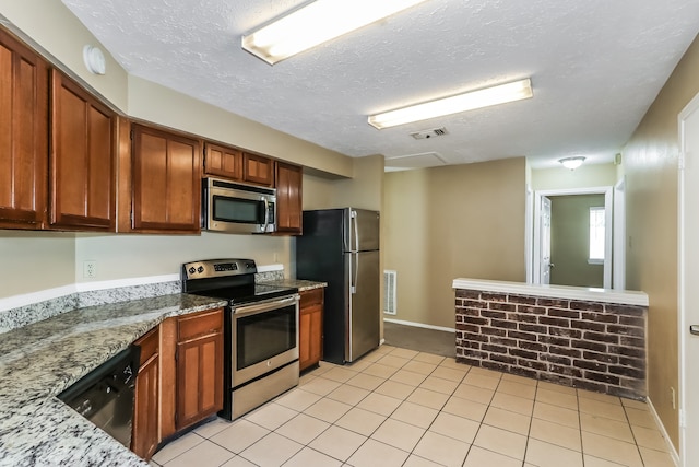 kitchen with light stone countertops, appliances with stainless steel finishes, light tile patterned floors, and a textured ceiling