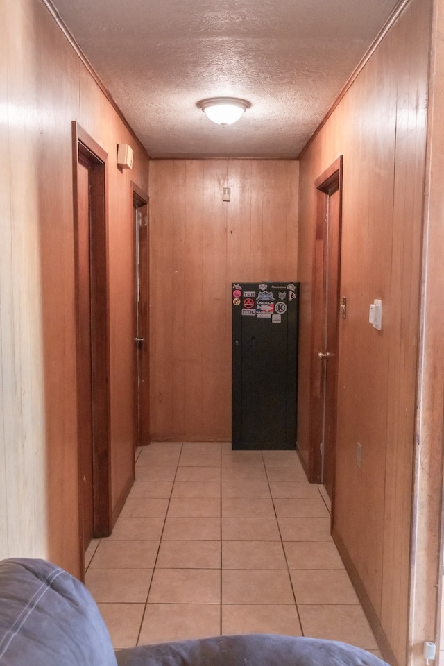 hall with light tile patterned flooring, wooden walls, and a textured ceiling