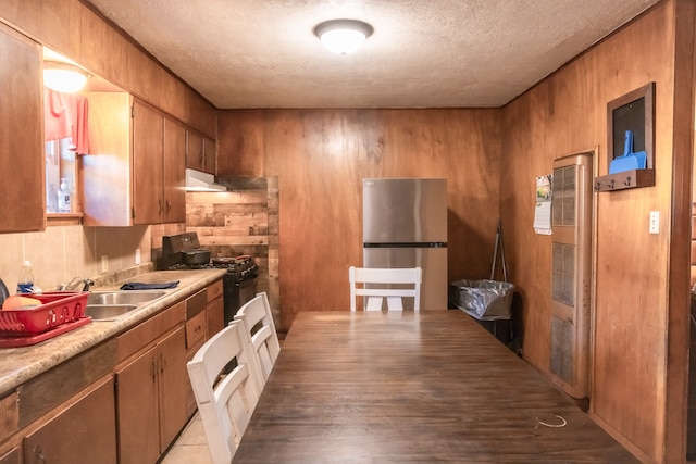 kitchen with wood walls, stainless steel refrigerator, black gas range, sink, and a textured ceiling