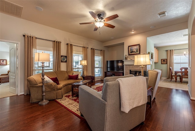 living room featuring dark hardwood / wood-style floors, a tiled fireplace, a wealth of natural light, and ceiling fan