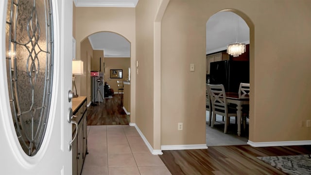 corridor with ornamental molding, light wood-type flooring, and a notable chandelier