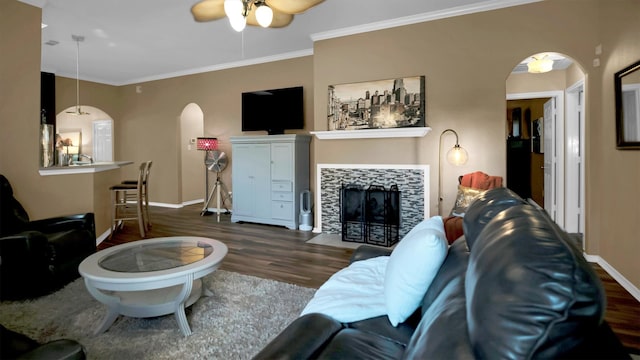 living room with ornamental molding, dark hardwood / wood-style floors, a tiled fireplace, and ceiling fan