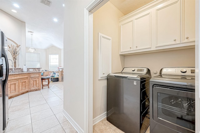 clothes washing area with cabinets, light tile patterned floors, and washer and clothes dryer