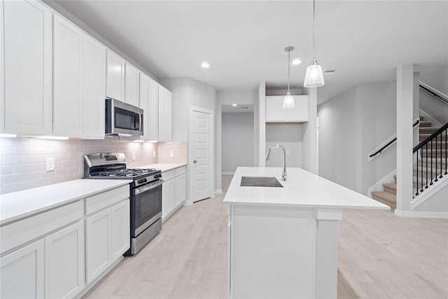 kitchen featuring sink, white cabinetry, hanging light fixtures, a center island with sink, and appliances with stainless steel finishes