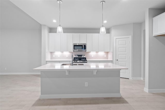 kitchen featuring an island with sink, appliances with stainless steel finishes, sink, and decorative light fixtures