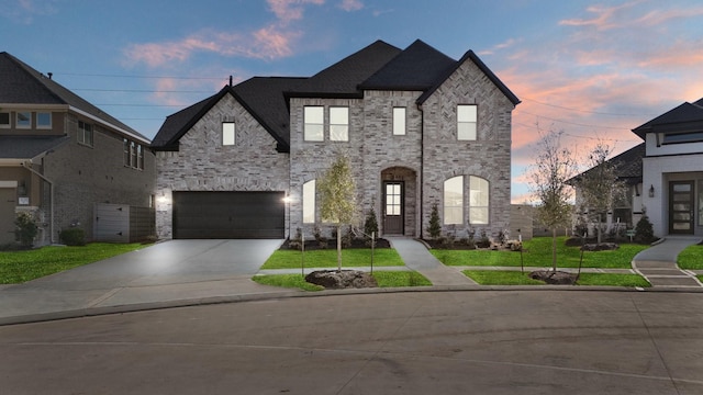 french provincial home featuring a garage, concrete driveway, brick siding, and a lawn