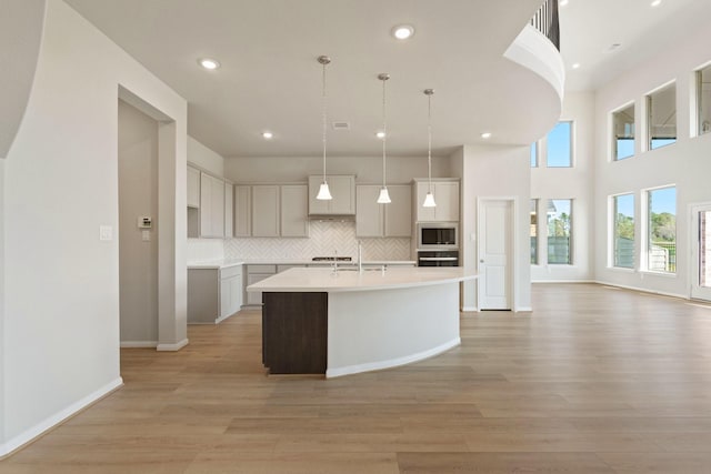 kitchen with oven, built in microwave, light wood-style floors, decorative backsplash, and a center island with sink