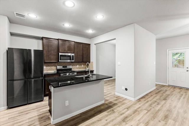 kitchen with light wood-type flooring, tasteful backsplash, a center island with sink, sink, and stainless steel appliances