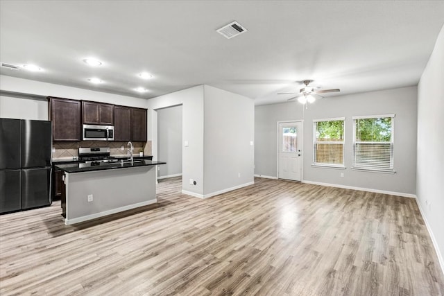 kitchen with ceiling fan, a kitchen island with sink, backsplash, stainless steel appliances, and light hardwood / wood-style floors