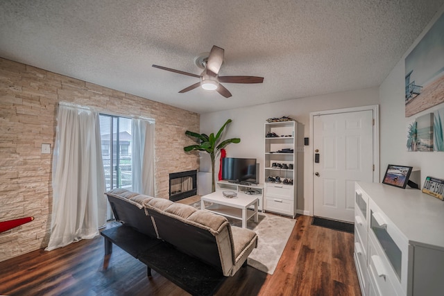 living room with a fireplace, ceiling fan, dark hardwood / wood-style floors, and a textured ceiling