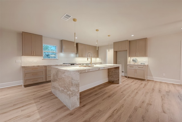 kitchen featuring light stone counters, a kitchen island with sink, sink, light hardwood / wood-style floors, and decorative light fixtures