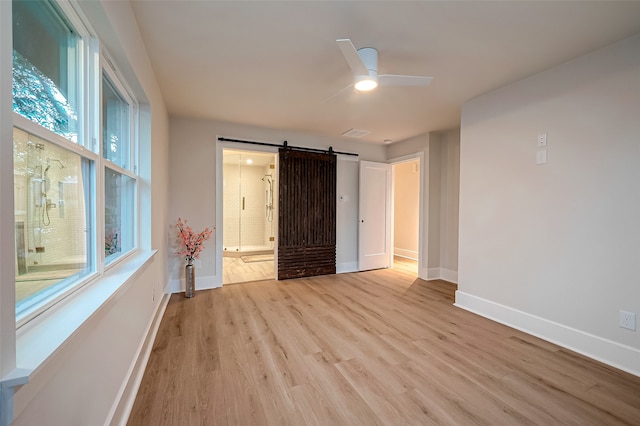 unfurnished bedroom featuring ensuite bath, a barn door, light wood-type flooring, and ceiling fan