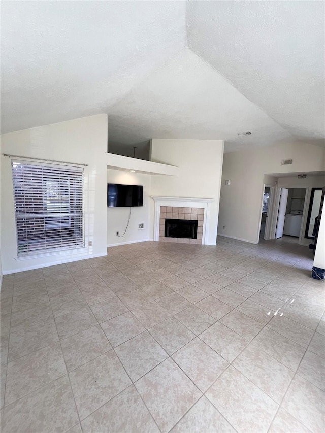 unfurnished living room with a textured ceiling, a tile fireplace, light tile patterned floors, and lofted ceiling