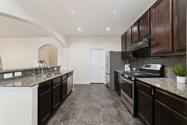 kitchen featuring light stone counters, dark brown cabinetry, sink, stainless steel appliances, and decorative backsplash