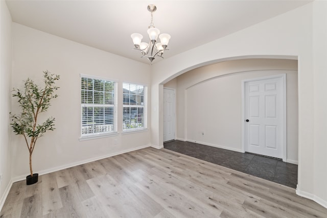 unfurnished room with a notable chandelier and light wood-type flooring