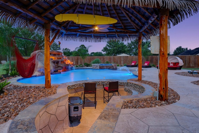 pool at dusk featuring a patio area, a gazebo, an in ground hot tub, and pool water feature