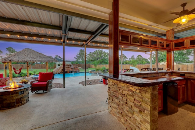 patio terrace at dusk featuring ceiling fan, a wet bar, a gazebo, and an outdoor fire pit