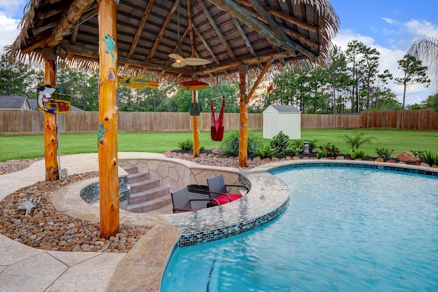 view of pool featuring ceiling fan, a gazebo, a yard, and a storage unit