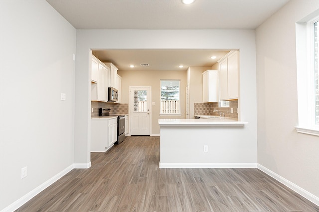 kitchen with decorative backsplash, light hardwood / wood-style flooring, white cabinets, and appliances with stainless steel finishes