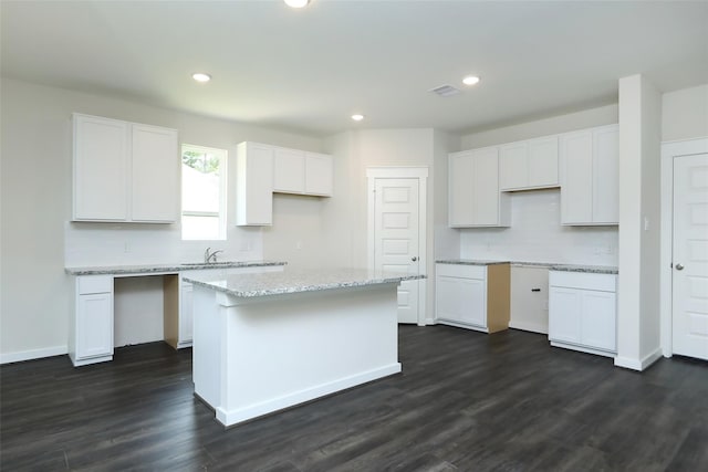 kitchen with light stone counters, sink, white cabinetry, a center island, and dark hardwood / wood-style flooring