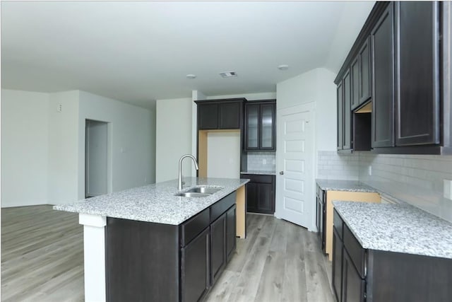 kitchen with light stone counters, sink, a center island with sink, light hardwood / wood-style floors, and decorative backsplash