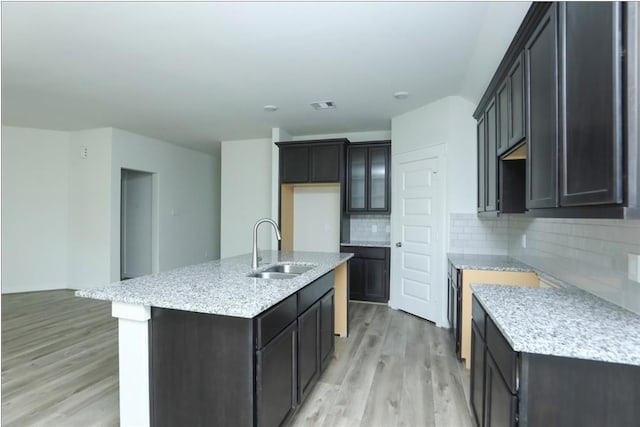 12135 Mustang Ave, Willis, TX 77378 - kitchen with a sink, light wood-type flooring, backsplash, a kitchen island with sink, and light stone counters