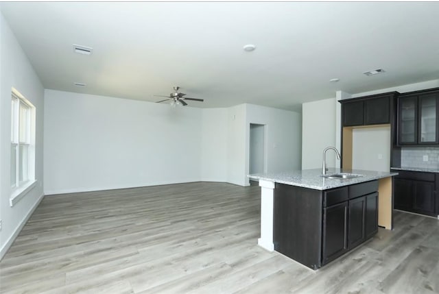 kitchen featuring light stone countertops, an island with sink, light hardwood / wood-style floors, and sink