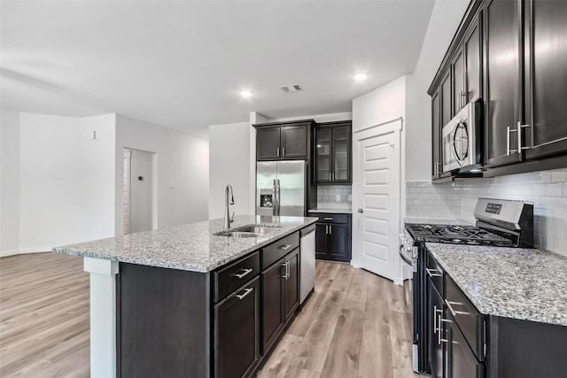 12135 Mustang Ave, Willis, TX 77378 - kitchen with appliances with stainless steel finishes, light wood-type flooring, an island with sink, backsplash, and light stone countertops