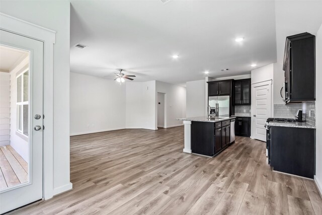 12135 Mustang Ave, Willis, TX 77378 - kitchen featuring stainless steel fridge with ice dispenser, light wood-style flooring, a center island with sink, ceiling fan, and dark cabinetry