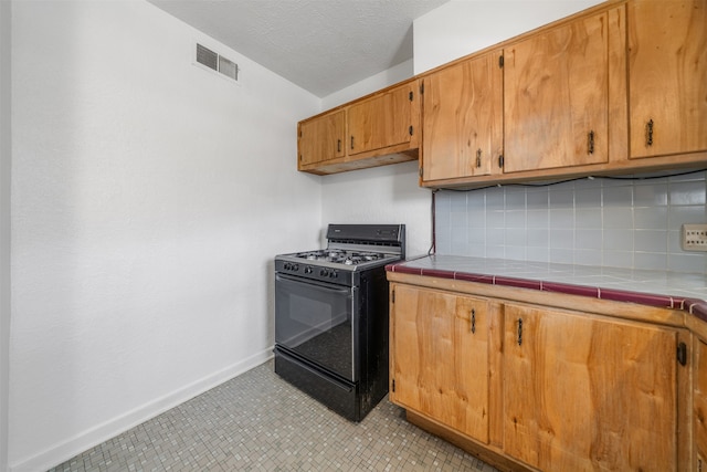 kitchen featuring tile countertops, gas stove, decorative backsplash, and a textured ceiling