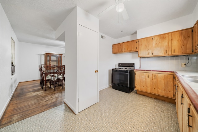 kitchen with ceiling fan, tasteful backsplash, black range with gas stovetop, light hardwood / wood-style flooring, and a textured ceiling