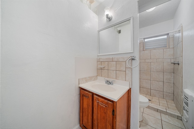 bathroom with tiled shower, vanity, tile patterned flooring, and toilet