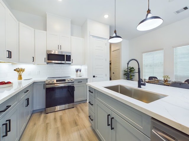 kitchen with gray cabinets, light hardwood / wood-style flooring, sink, stainless steel appliances, and hanging light fixtures