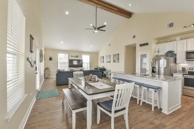 dining area featuring high vaulted ceiling, ceiling fan, beamed ceiling, and light hardwood / wood-style flooring