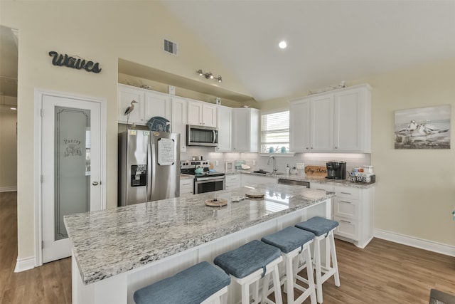 kitchen featuring sink, a kitchen island, white cabinetry, appliances with stainless steel finishes, and a kitchen breakfast bar