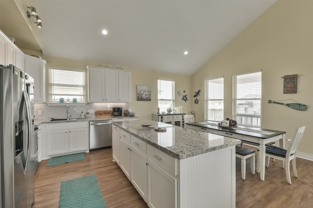 kitchen with light wood-type flooring, a kitchen island, white cabinetry, appliances with stainless steel finishes, and light stone countertops