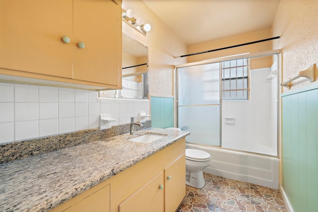 full bathroom with decorative backsplash, toilet, shower / bath combination with glass door, and vanity