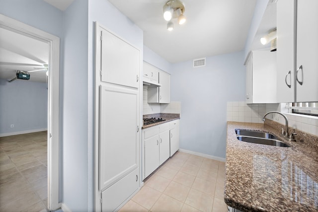 kitchen featuring stainless steel gas stovetop, sink, decorative backsplash, dark stone countertops, and white cabinetry