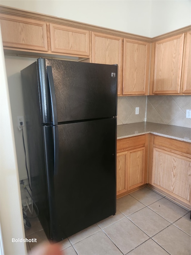 kitchen featuring light brown cabinetry, black refrigerator, backsplash, and light tile patterned floors