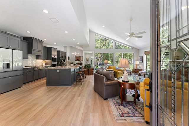 living room with high vaulted ceiling, ceiling fan, and light hardwood / wood-style flooring